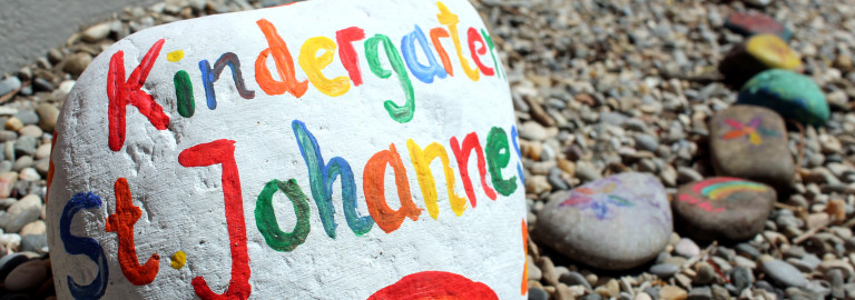 Ein Stein mit Regenbogen und der Aufschrift "Kindergarten St. Johannes"